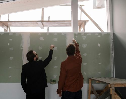 Two men discussing and pointing at an interior wall during a renovation project.
